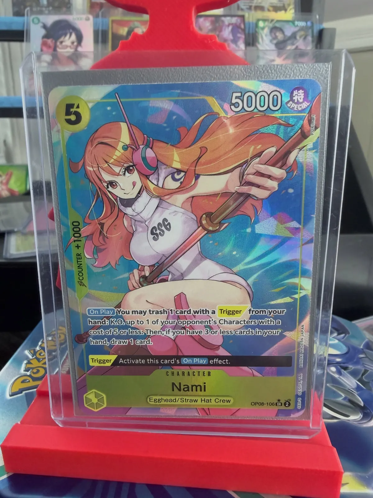 A One Piece Nami card in a top loader on a red display stand