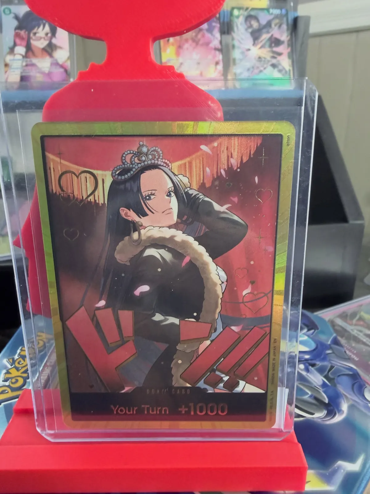 A foil One Piece Nico Robin card in a top loader on a red display stand