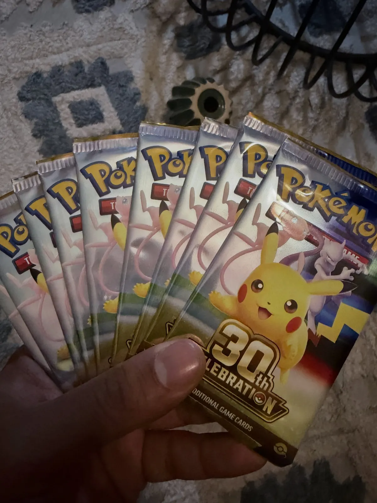 A hand holding a fan of sealed Pokémon 30th Celebration booster packs with Pikachu on the front