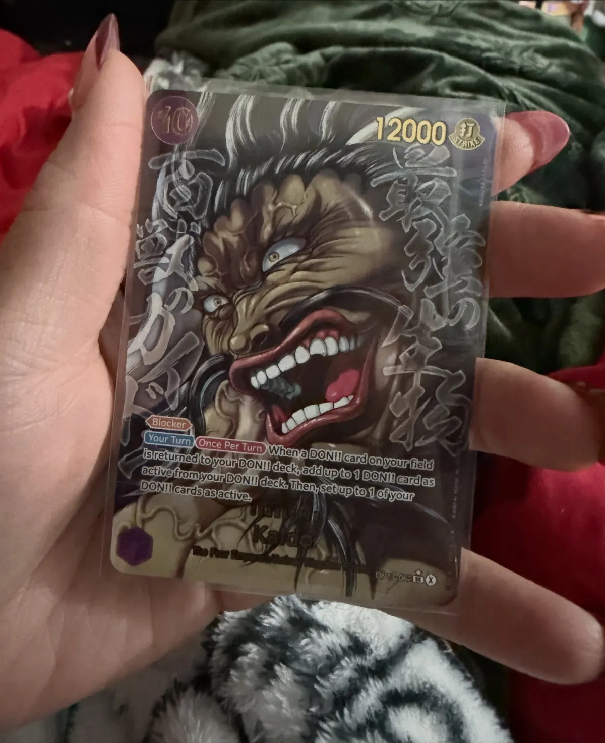 A hand holding a black-and-gold One Piece Kaido card pulled from a pack